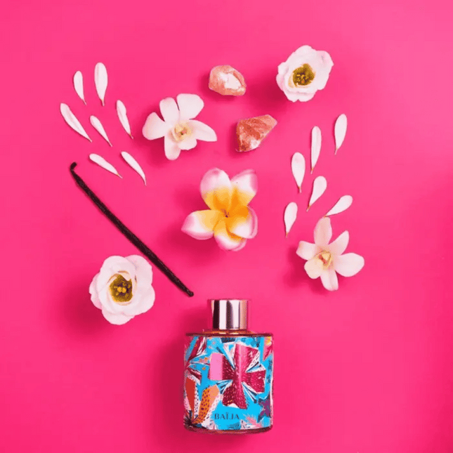 Perfume bottle with colorful design surrounded by flowers on a pink background